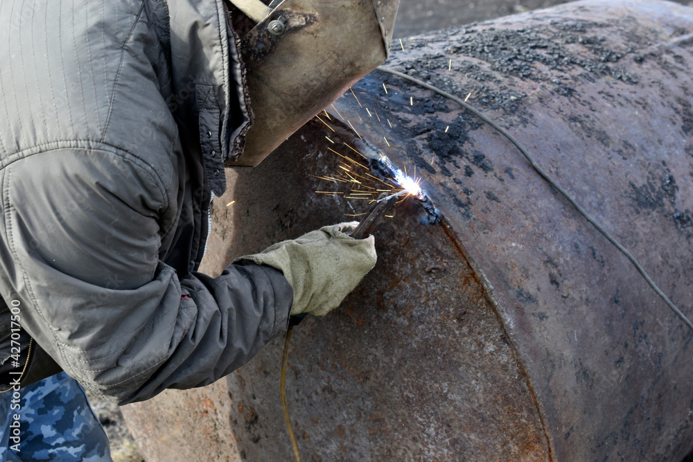 A worker welding an iron pipe with a protective mask A worker welding an iron pipe with a protective mask