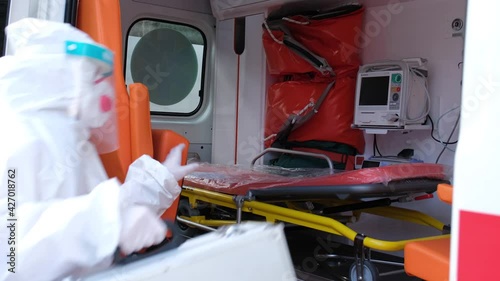 Female doctor Wearing a Transparent Protective Face Shield, Mask and Overalls at the Covid-19 gets into ambulance car. Ambulance crew gets into transport, ready to save lives, responds to call out.
