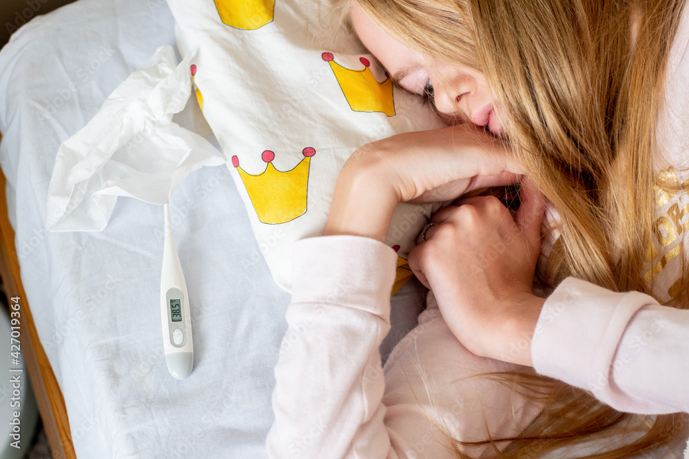 Sick teenage girl lying on the bed covered with blanket with ...