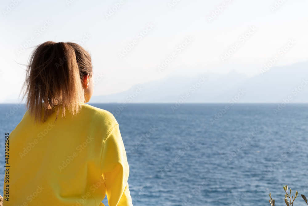 Concept of calmness, serenity and tranquility. Young girl sits on sea shore looks in distance and dreaming.  Dreams come true.