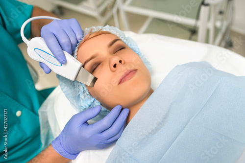 Close up cosmetologist hands in gloves making ultrasound cleaning procedure to the patient's face with perfect skin.