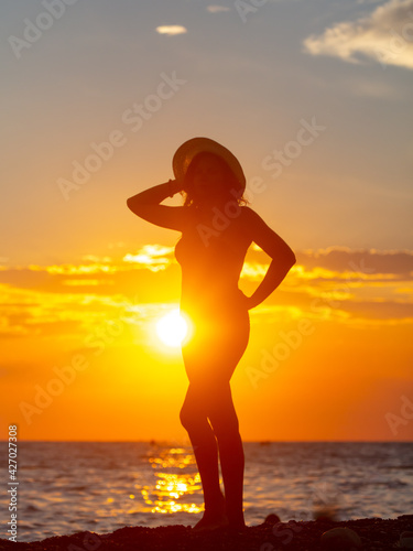 Silhouette of a girl in a swimsuit with a hat near the sea
