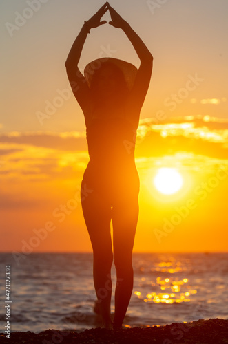 Silhouette of a girl in a swimsuit with a hat near the sea