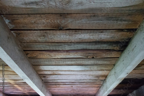 Grunge rough wooden ceiling in a perspective view with colorful stains of fungus and moist and jars in wood. Beamed ceiling in a shed or attic or old wooden cabin.