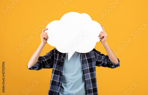 Unrecognizable young man holding blank speech bubble in front of his face over orange background, mockup for design