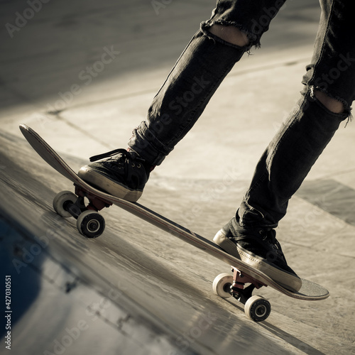 Close up view of tennager's feet riding a skateboard making tricks on half pipe. Trendy young skater enjoying outdoors at the skatepark with skate board. Youth, freedom, sport joy and carefree concept