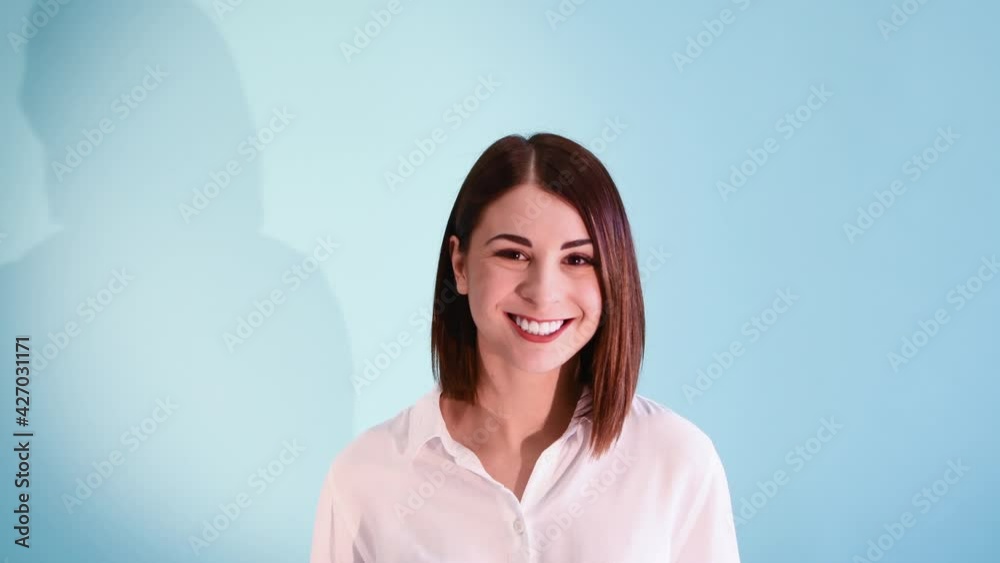 Beautiful caucasian woman with brown hair wearing white shirt starts to smile against blue background. White teeth smile. 4K Resolution video. Beautiful caucasian woman with brown hair wearing white shirt starts to smile against blue background. White teeth smile. 4K Resolution video.