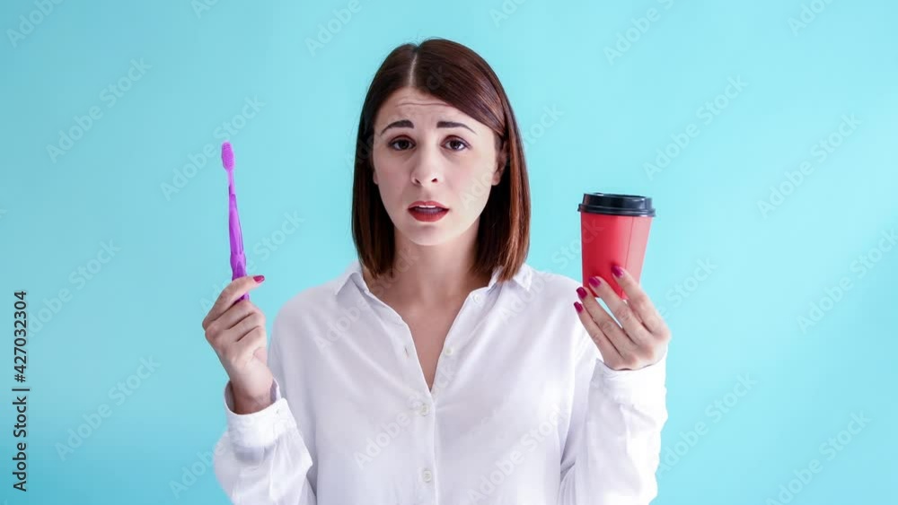 Beautiful caucasian woman in white shirt holds red paper cup in one hand and manual purple toothbrush in other. Blue background. 4K resolution video. Dental Health Theme. Beautiful caucasian woman in white shirt holds red paper cup in one hand and manual purple toothbrush in other. Blue background. 4K resolution video. Dental Health Theme.