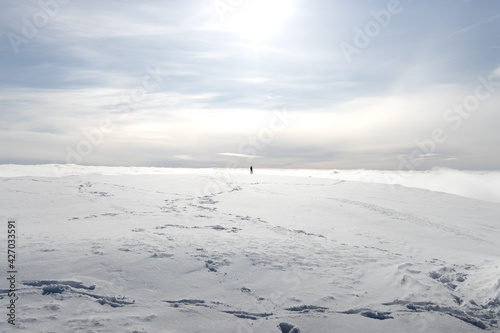 person walking alone on mountain above clouds in ski resort under the sun