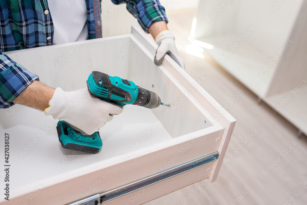 Furniture assembler assembles a cabinet shelf, from the inside, using an electric screwdriver, close-up