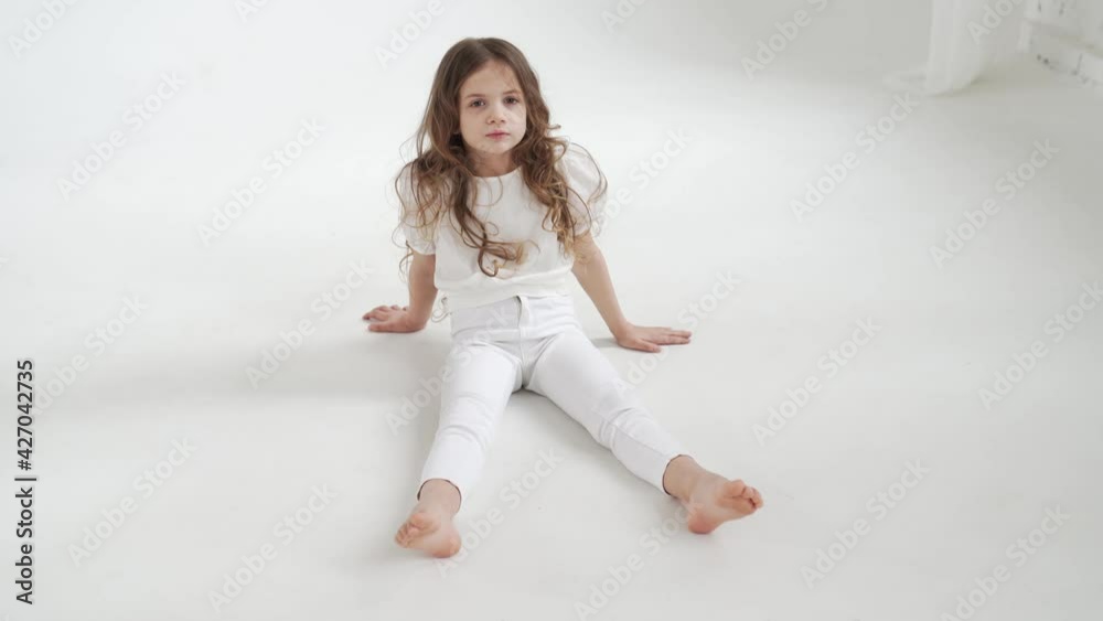 beautiful little girl with long hair in white clothes sits on the floor. beautiful little girl with long hair in white clothes sits on the floor.
