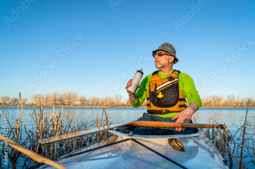senior male in an expedition canoe is taking break for hydration, early spring scenery on a lake in northern Colorado, POV from boat bow
