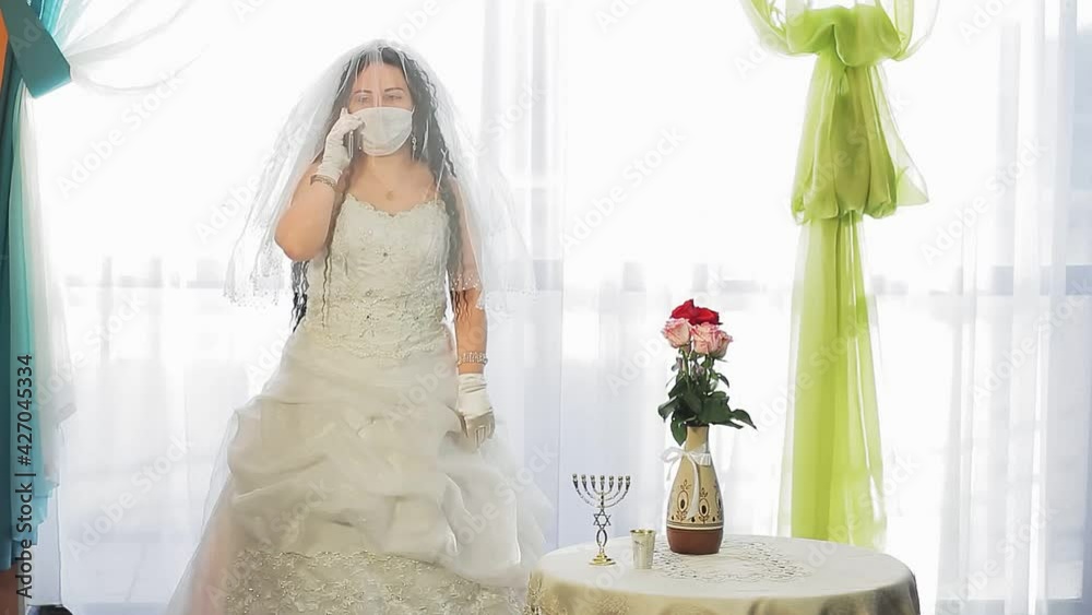 A Jewish bride in a wedding dress and a veil wearing a medical mask in