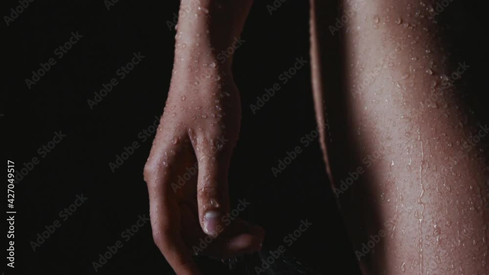 Drops of water flow down female hands and hips close up. Young woman gets wet in the rain alone. Cold helps to plunge into sad thoughts deeper. Broken girl in the black swimsuit froze from the cold.