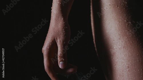 Drops of water flow down female hands and hips close up. Young woman gets wet in the rain alone. Cold helps to plunge into sad thoughts deeper. Broken girl in the black swimsuit froze from the cold.