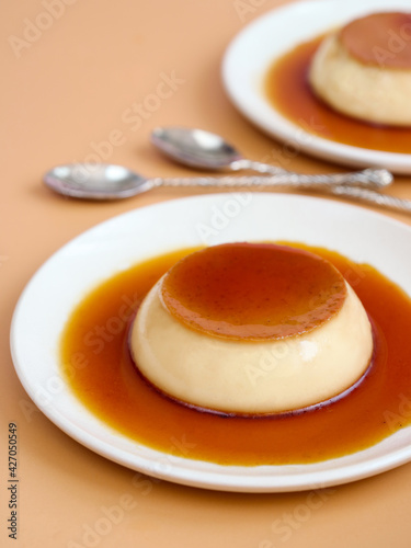 A caramel custard pudding with vanilla flavor in a white plate and spoon. It's a dessert base with caramelized sugar layer toppings which is made of eggs, sugar, milk who are the main ingredients