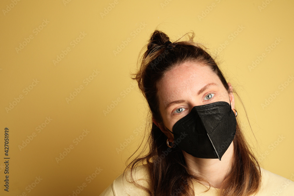 Close-up of young woman wearing black face mask isolated on yellow background. Close-up of young woman wearing black face mask isolated on yellow background.