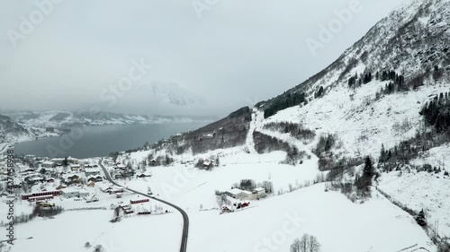 Drone shot of snowy mountains, Skei Village and natural lake in background during misty day in Norway. Aerial forward shot. Norwegian Travel resort in nature. photo