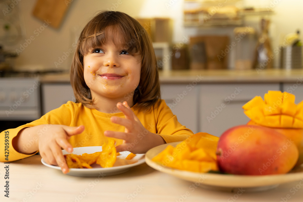 Cute child girl is happy to eat mangoes. Schoolgirl joy tasty eating ...