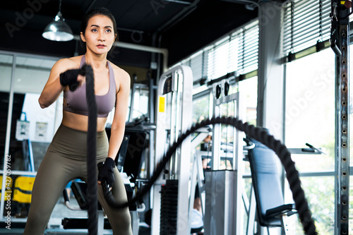 Young Asian girl in fitness gym. Asian woman working out in gym doing strength training working out with battle rope. Fitness woman exercising indoor in fitness center. Female with in gym.
