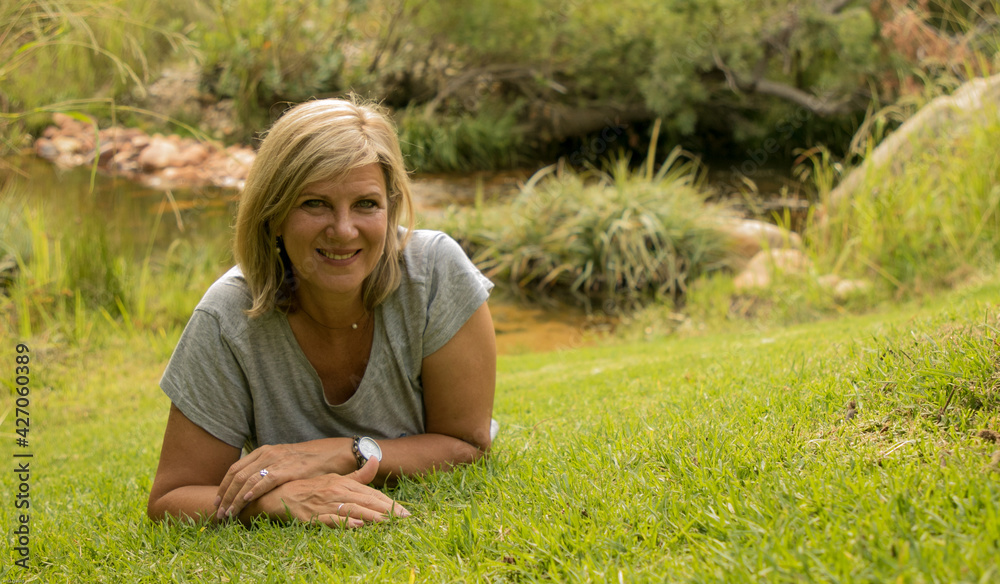 Attractive, mature woman lying on grass in nature Attractive, mature woman lying on grass in nature