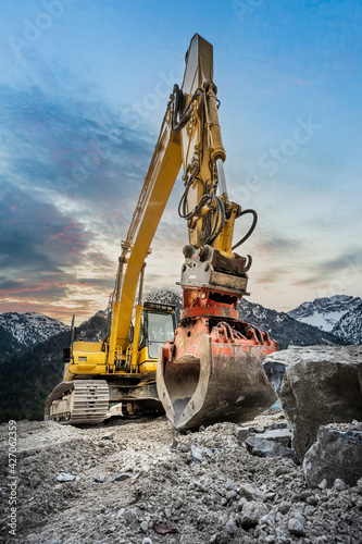 huge clamshell grab excavator for natural stone masonry in front of alp mountains and heavy rocks © A2LE