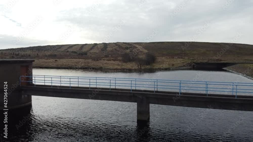 Aerial view flying over bridge to reservoir maintenance hut
