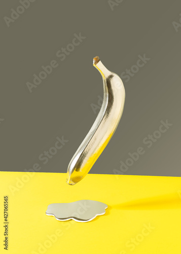 Minimal retro futurism with banana and silver liquid against gray and yellow background.