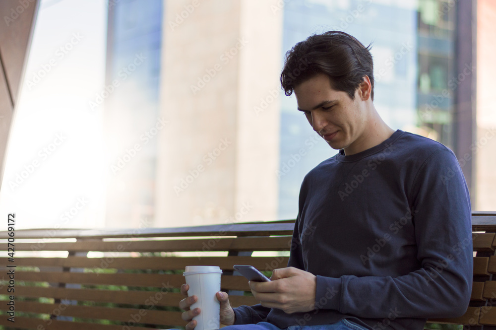 Young male in casual wear watching his mobile phone with bright smile and drinking coffee Young male in casual wear watching his mobile phone with bright smile and drinking coffee