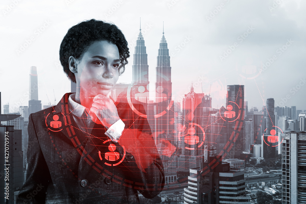 Fototapeta premium Attractive black HR director at international company is thinking about recruitment of highly qualified specialists. Women in business concept. Social media hologram icons over Kuala Lumpur.