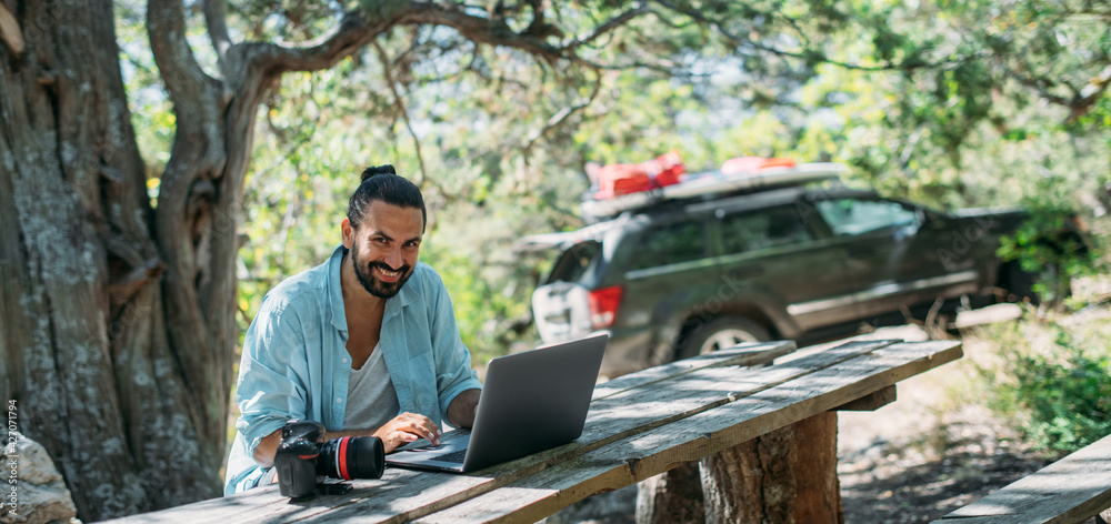 Male photographer working on a laptop outdoors in a camping Male photographer working on a laptop outdoors in a camping