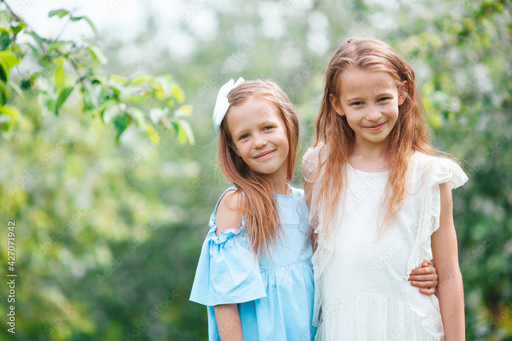 Adorable little girls in blooming apple tree garden on spring day Adorable little girls in blooming apple tree garden on spring day