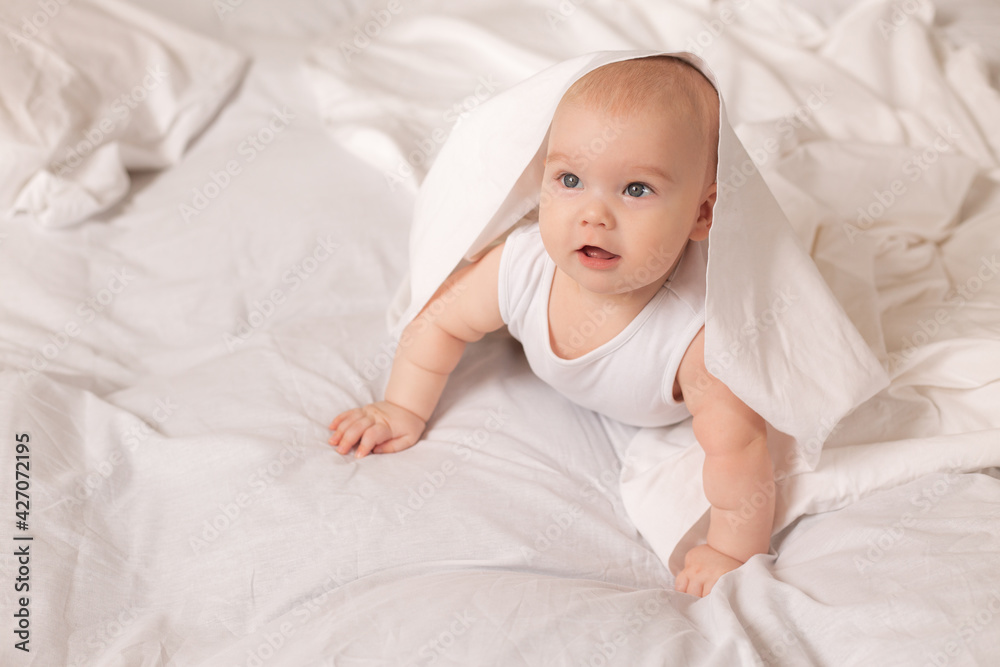 Cute toddler in white bodysuit lies in bed with white bedding Cute toddler in white bodysuit lies in bed with white bedding