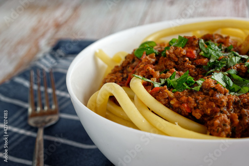 Close up of Italian pasta with bolognese, in a bowl. In the background a blue kitchen towel.