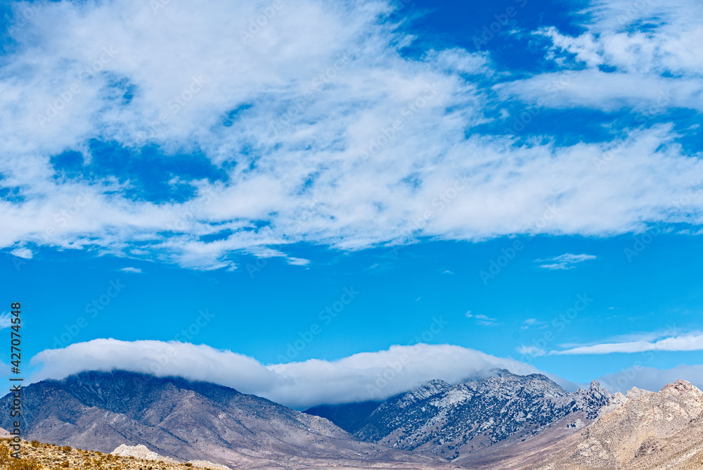 Blue brown mountains wrapped in a blanket of white clouds under a blue sky.