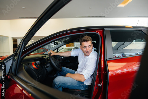A young man is sitting in the cabin of a new car and testing it. Buying a car © Andrii