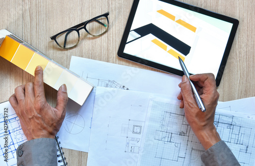 top view of architect working desk with hand writing and draw on equipment for drawings pens sketched idea on wood table, concept of modern technology for architectural working with tablet