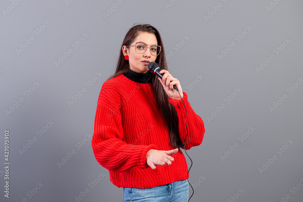 Obraz premium young, emotional brunette with a microphone dressed in a red sweater sings karaoke or says a speech