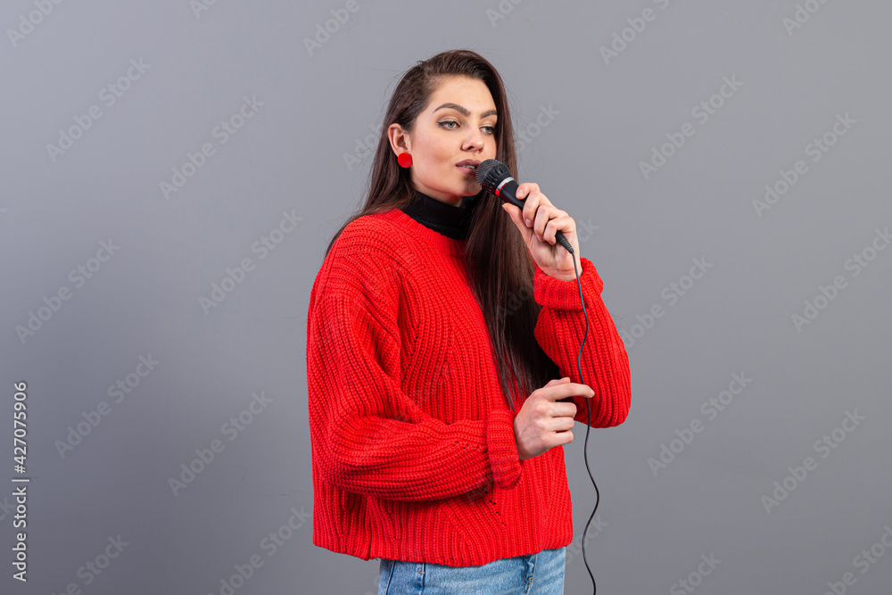Obraz premium young, emotional brunette with a microphone dressed in a red sweater sings karaoke or says a speech