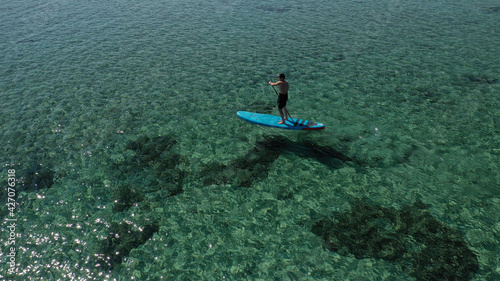 Aerial drone photo of fit man practising Stand Up Paddle or SUP in tropical exotic lake with shallow emerald water © aerial-drone