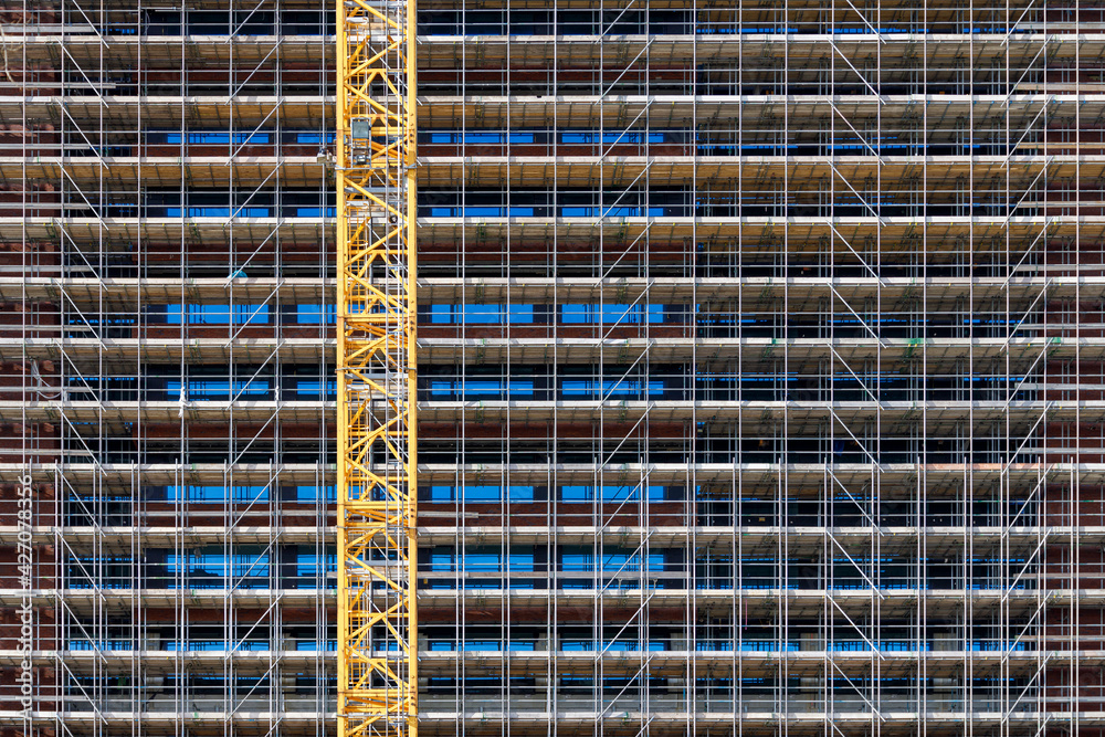 huge scaffolding covering the facade of a tall building and a yellow crane in front huge scaffolding covering the facade of a tall building and a yellow crane in front