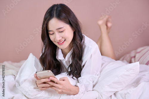 Young smiling Asian woman using smartphone for play game or buying online shopping