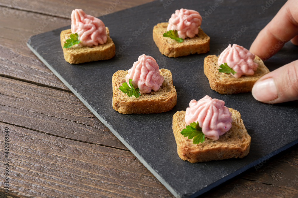 Hand takes crostini or canapes with taramasalata from a slate board
