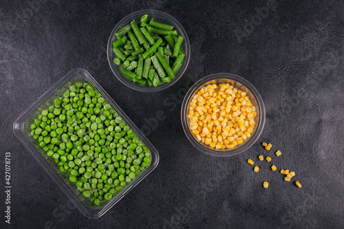 Plastic container with different organic deep frozen vegetables on a black table