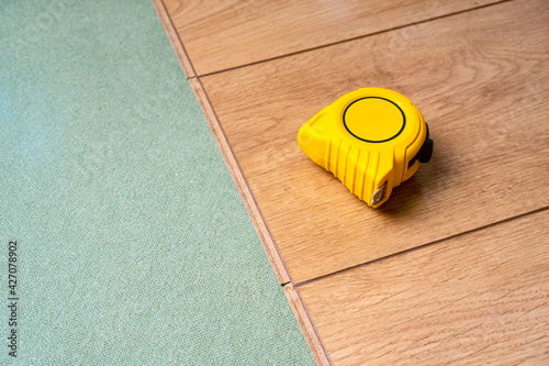 High-quality laminate floor installing. Natural underlay for laminate. Yellow measure tape lies on top. Copy space.