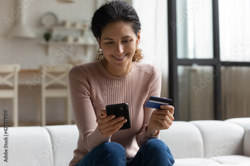 Safe mobile banking. Smiling latina lady client hold mobile phone credit bank card do online shopping provide internet payment. Happy young woman enjoy easy fast secure transferring money in ebank app photo