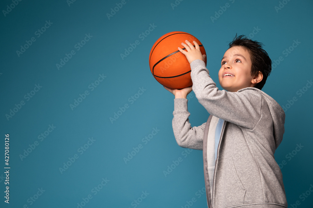 Adorable boy playing basketball on blue background with space for text Adorable boy playing basketball on blue background with space for text