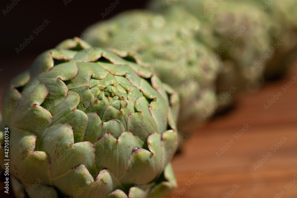 Fototapeta premium Close-up of an artichoke, behind which other artichokes are lined up on a wooden surface