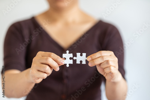 Closeup of woman hand holding and connecting two white paper jigsaw puzzle. Using as Business solutions and strategy concept.