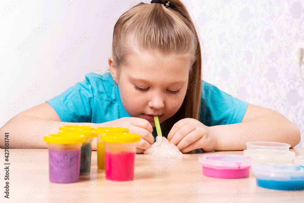 A blonde-haired child inflates a bubble of white mucus. Play a slime toy. Making slime at home A blonde-haired child inflates a bubble of white mucus. Play a slime toy. Making slime at home